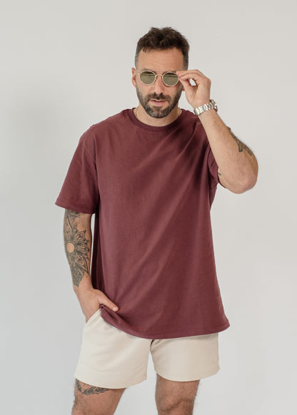 Man wearing a maroon t-shirt and beige shorts on a white background