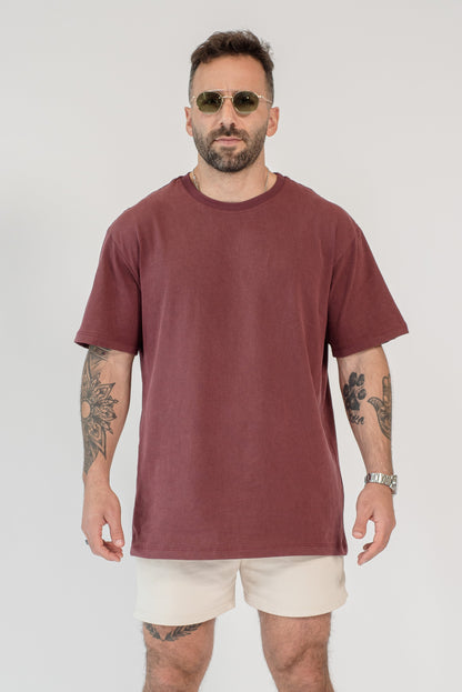 Man wearing a maroon t-shirt and beige shorts on a white background