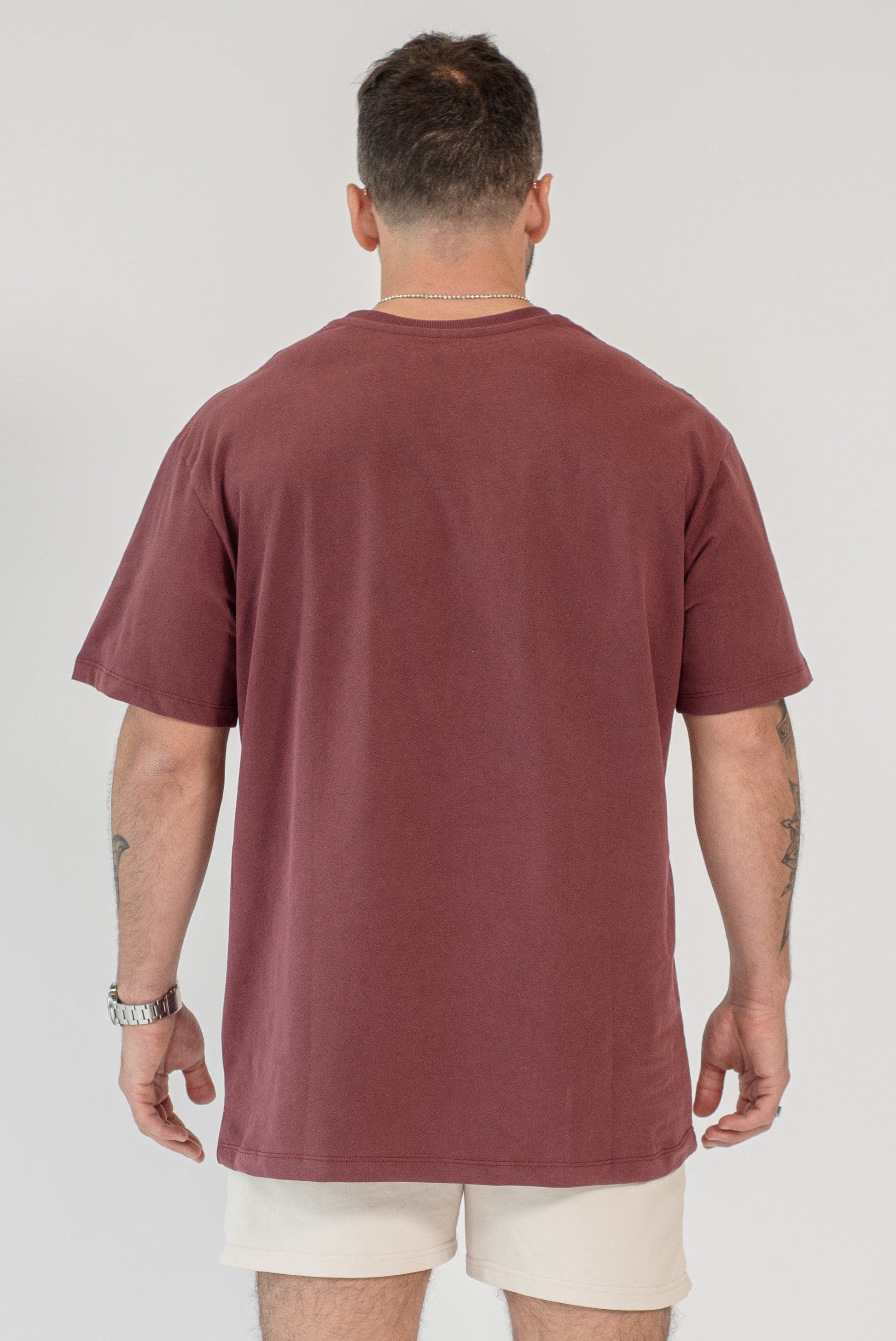 Man wearing a maroon t-shirt and beige shorts on a white background
