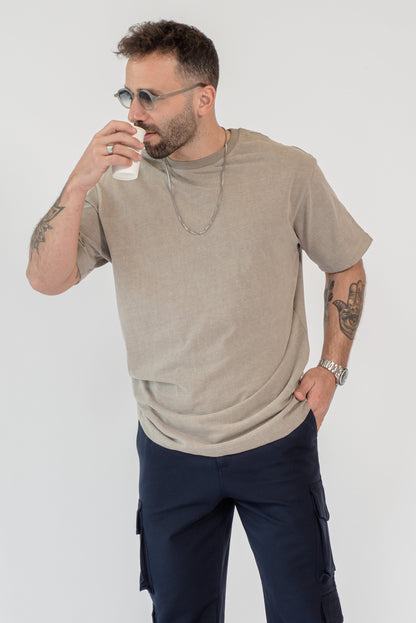 Man wearing a beige t-shirt and navy pants on a white background