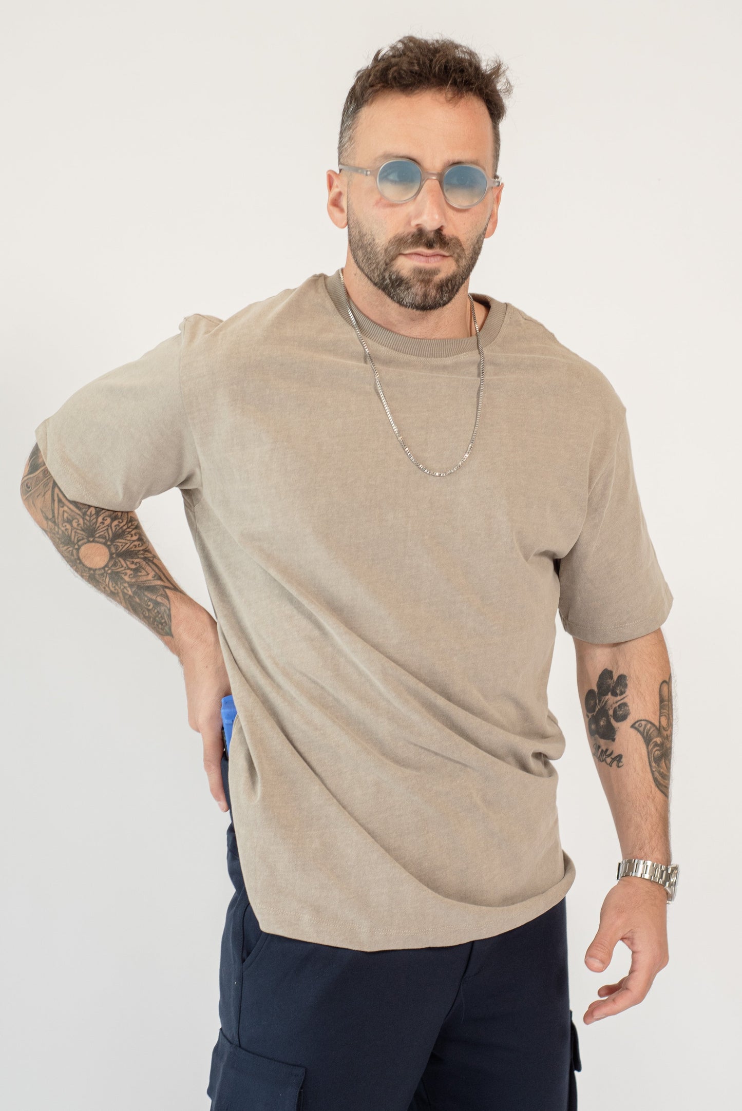 Man wearing a beige t-shirt and dark pants on a white background