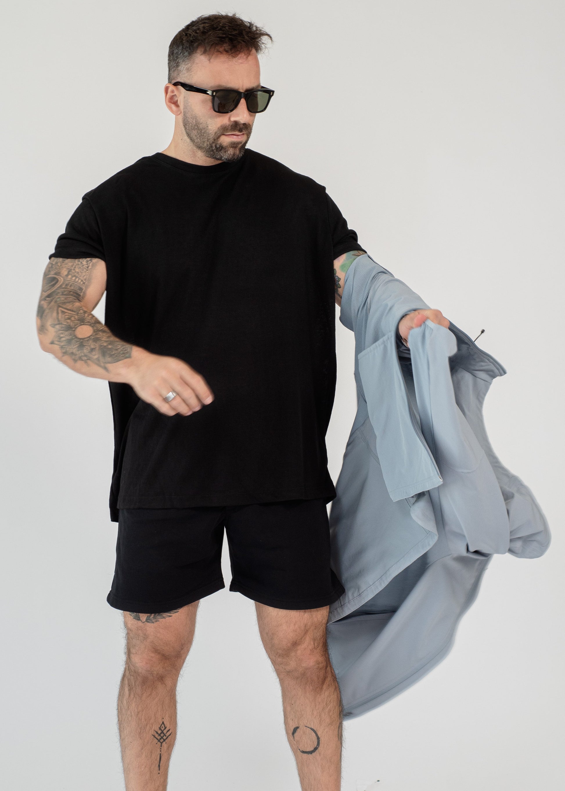 Man wearing a black outfit holding a gray jacket on a white background
