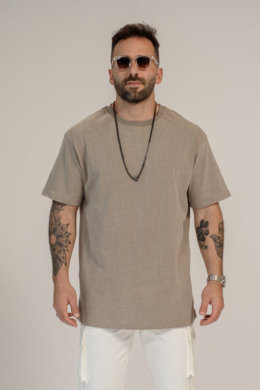 Man wearing a beige t-shirt, white pants, and sunglasses on a plain background