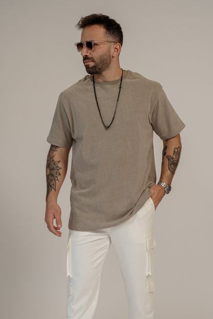 Man wearing a beige t-shirt and white pants against a plain background