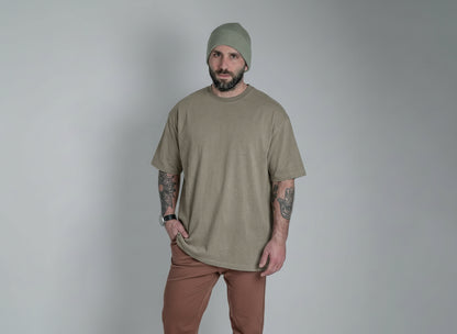 Man wearing a beige t-shirt and pants with a beanie against a gray background